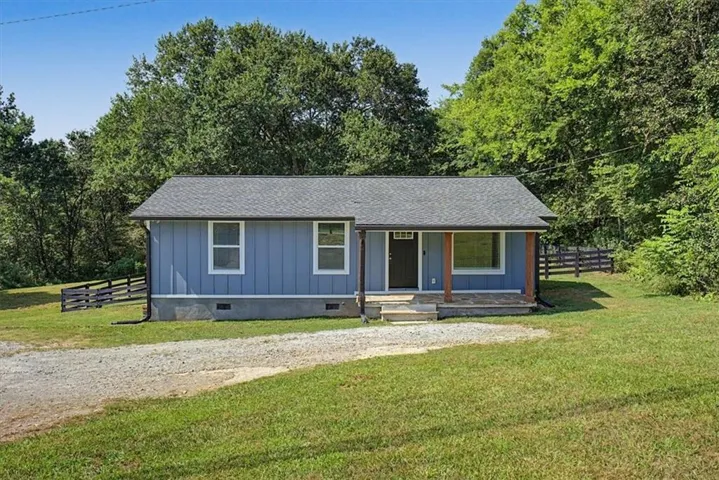 Ranch-style exterior with blue vertical siding, a dark gray roof, and a gravel driveway