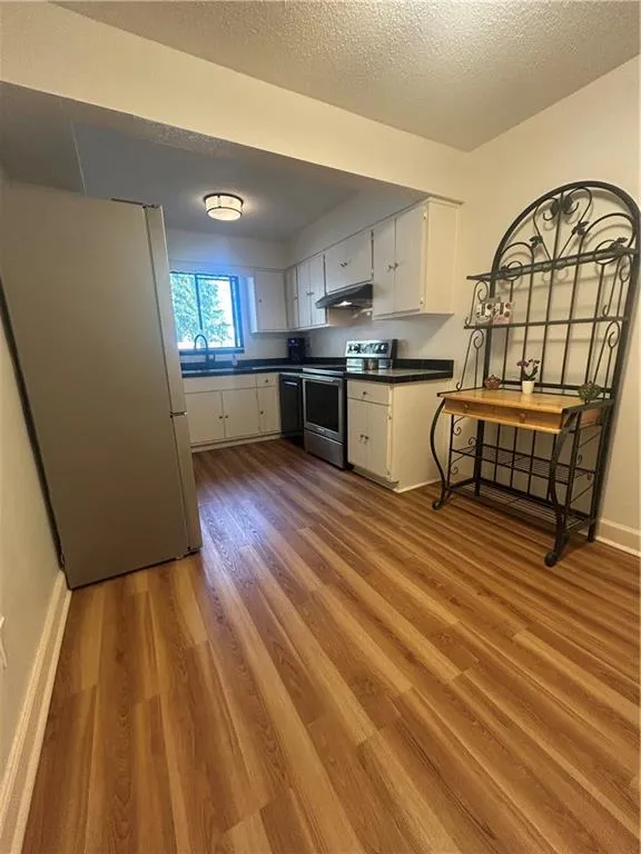 Kitchen with white cabinets, range, dark countertops, fridge, and exhaust hood