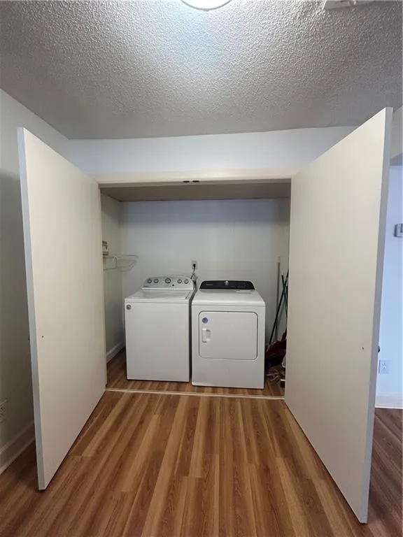 Laundry room featuring washer and dryer, laundry area, a textured ceiling, and wood finished floors