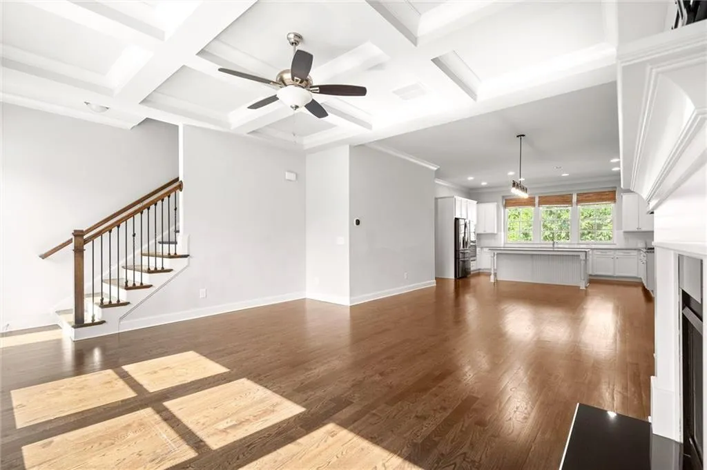 Unfurnished living room with a ceiling fan, coffered ceiling, beam ceiling, wood finished floors, and stairway