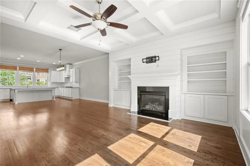 Unfurnished living room with built in shelves, ornamental molding, dark wood-style floors, coffered ceiling, and ceiling fan