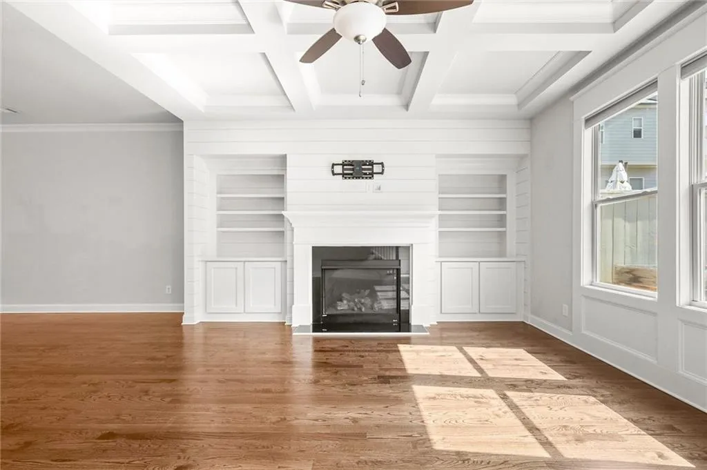 Unfurnished living room featuring wood finished floors, crown molding, ceiling fan, coffered ceiling, and beamed ceiling