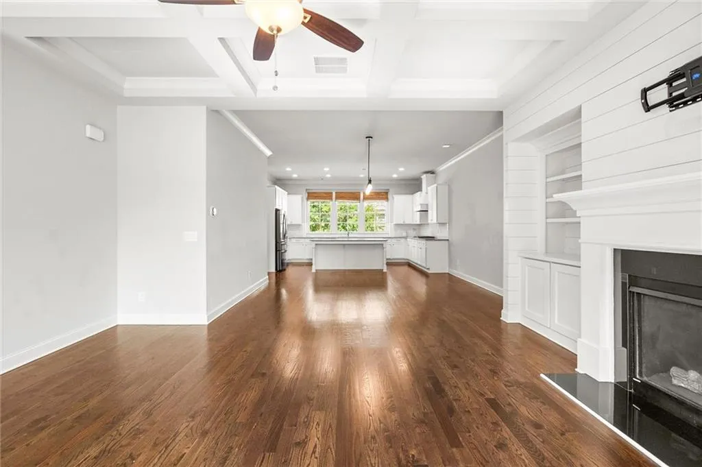 Unfurnished living room with ceiling fan, built in features, dark wood-style floors, a fireplace with raised hearth, and coffered ceiling
