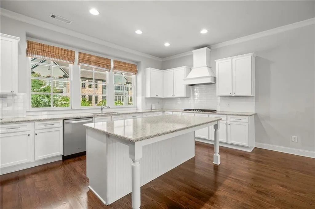 Kitchen featuring backsplash, crown molding, stainless steel dishwasher, white cabinets, and a kitchen island