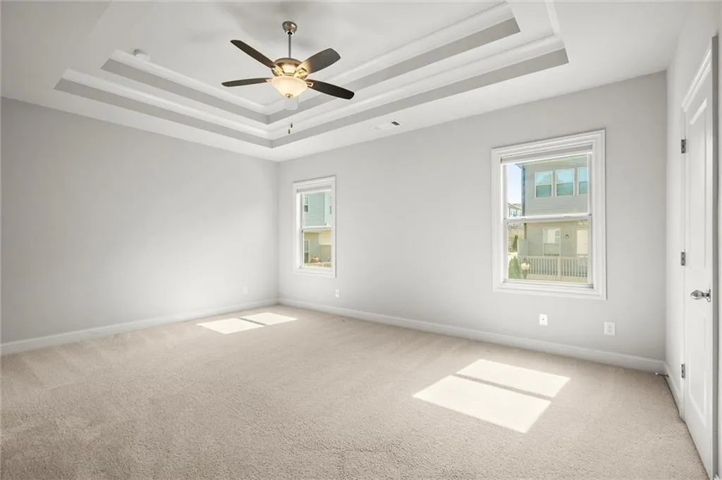 Empty room featuring a tray ceiling, carpet, and a ceiling fan