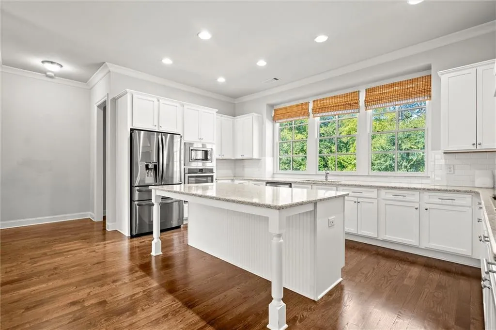 Kitchen with ornamental molding, appliances with stainless steel finishes, backsplash, dark wood-style flooring, and white cabinets