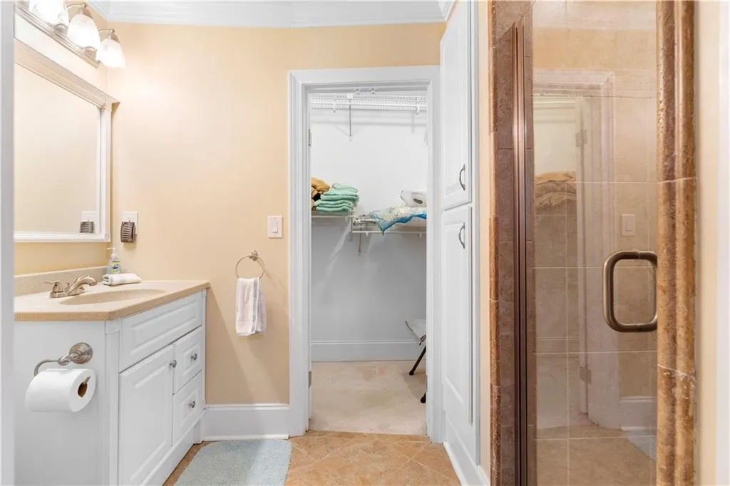 Bathroom with a spacious closet, vanity, a stall shower, ornamental molding, and light tile patterned flooring
