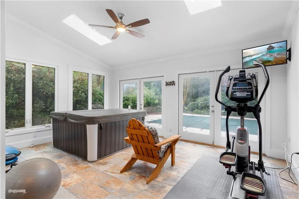 Sunroom with a skylight, stone tile floors, a hot tub and lofted ceiling