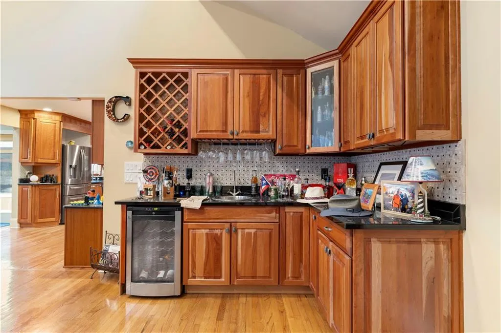 Indoor wet bar with wood finish cabinetry, wine cooler, light wood finished floors, and vaulted ceiling