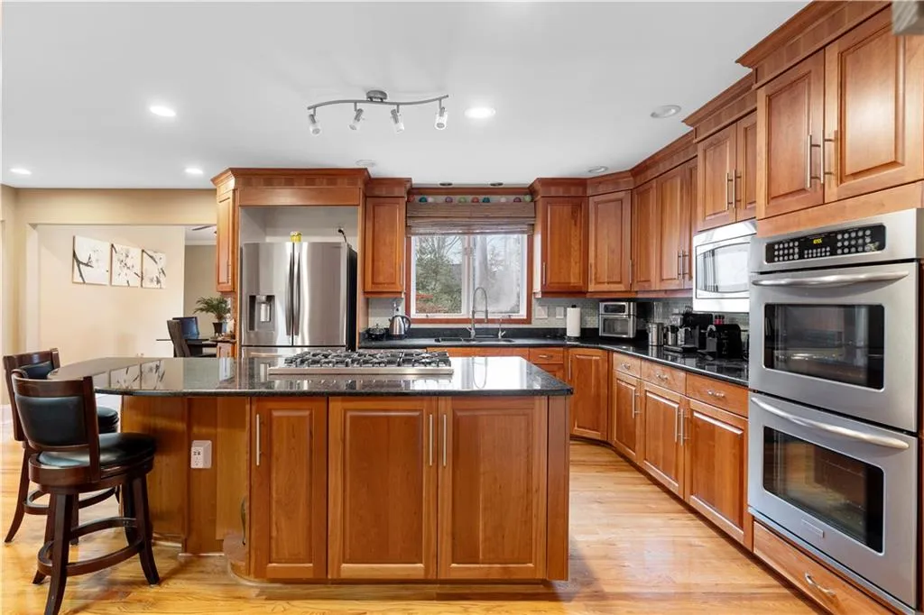 Kitchen featuring stainless steel appliances, wood finish cabinetry, dark stone countertops, a kitchen island, and backsplash