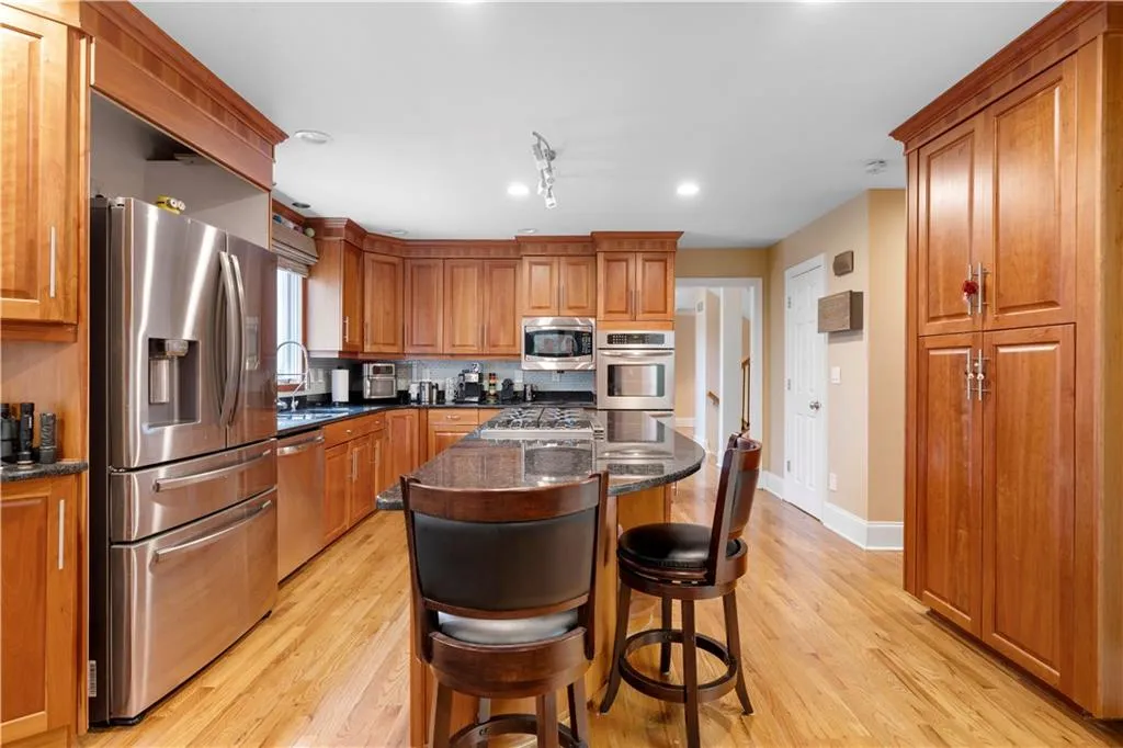 Kitchen featuring a kitchen bar, stainless steel appliances, wood finish cabinetry, dark stone counters, and a center island