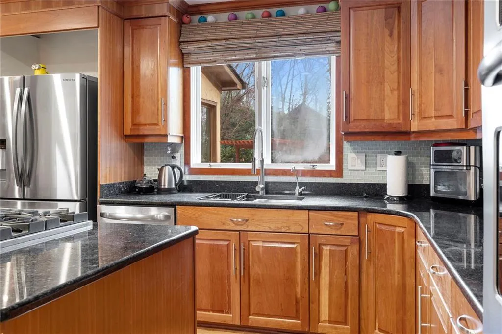 Kitchen featuring wood finish cabinets, stainless steel appliances, dark stone counters, and decorative backsplash