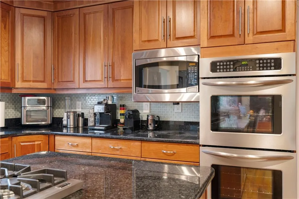 Kitchen featuring stainless steel appliances, wood finish cabinets, dark stone counters, and decorative backsplash