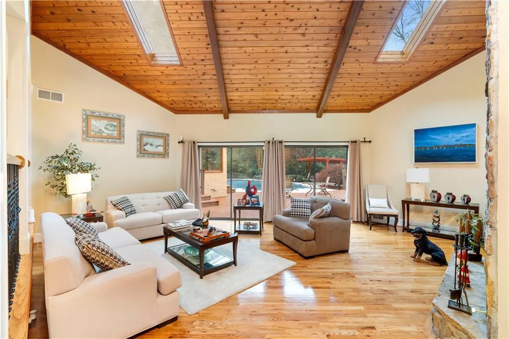 Living area with a vaulted wood ceiling, a skylight, hardwood finished floors and pool access