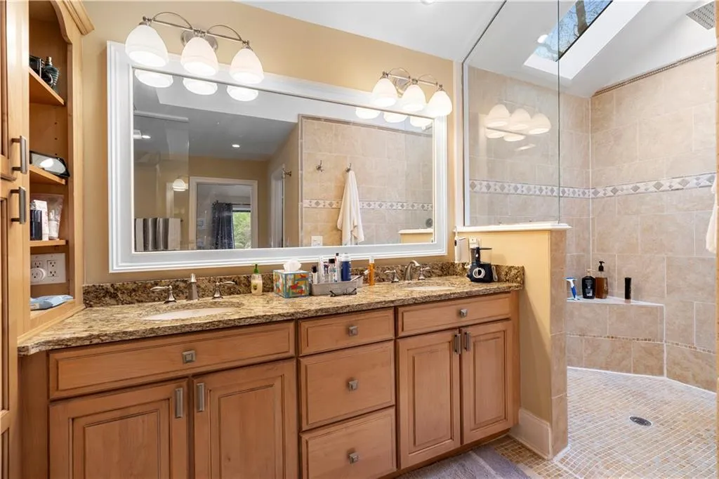 Main bathroom featuring a walk in shower, double vanity, and a skylight
