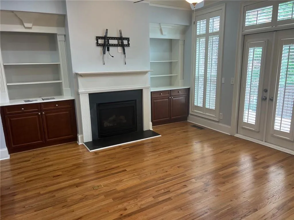 Unfurnished living room featuring light wood finished floors, built in shelves, a fireplace with raised hearth, and plenty of natural light