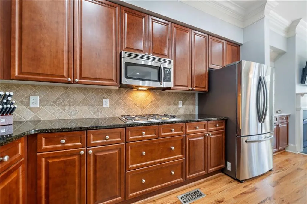 Kitchen featuring stainless steel appliances, ornamental molding, light wood-style floors, decorative backsplash, and dark stone counters
