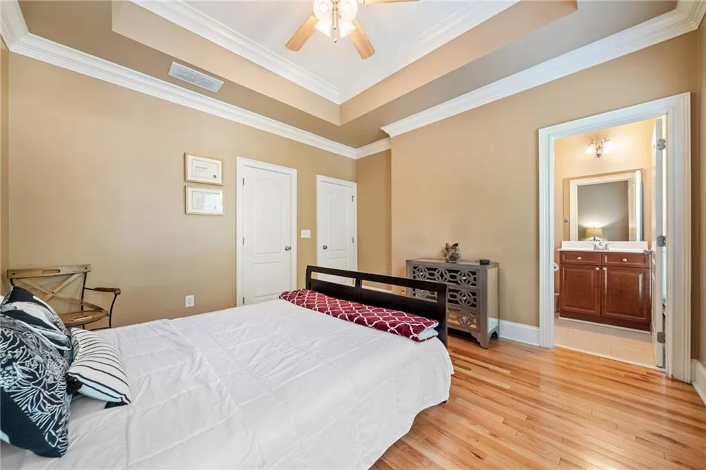 Bedroom featuring a tray ceiling, light wood-type flooring, ornamental molding, baseboards, and ensuite bathroom
