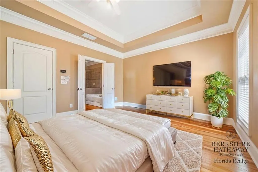 Virtually Staged Owners Bedroom with baseboards, a tray ceiling, multiple windows, ornamental molding, and wood finished floors