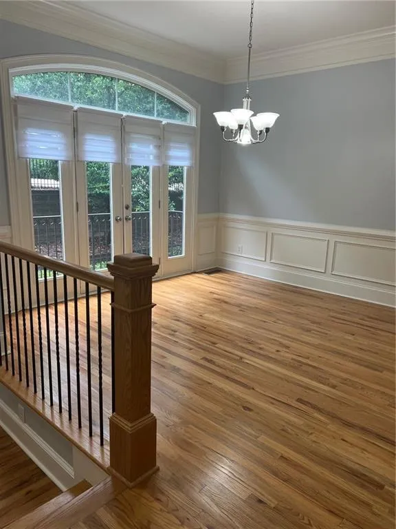 Currently Empty room with a chandelier, ornamental molding, wood finished floors, a wainscoted wall, and french doors