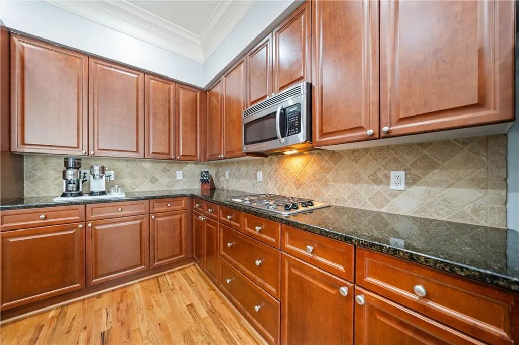 Kitchen featuring appliances with stainless steel finishes, crown molding, light wood-style flooring, dark stone countertops, and decorative backsplash