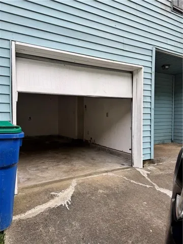 Garage featuring a partially open overhead door, concrete flooring, and light blue horizontal siding