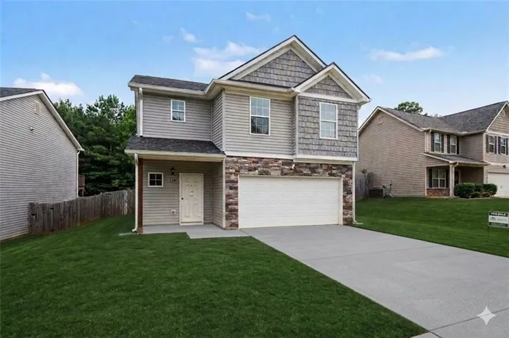 Two-story residence featuring siding and stone veneer accents, an attached garage, a concrete driveway, and a front porch