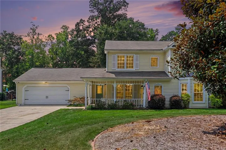 Two-story Colonial-style home featuring a front-load garage, covered front porch with railings, and multiple windows with yellow-trimmed frames