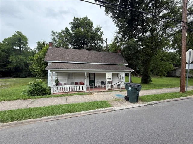 Classic white siding exterior with a dark shingled roof, featuring a covered porch with a white railing