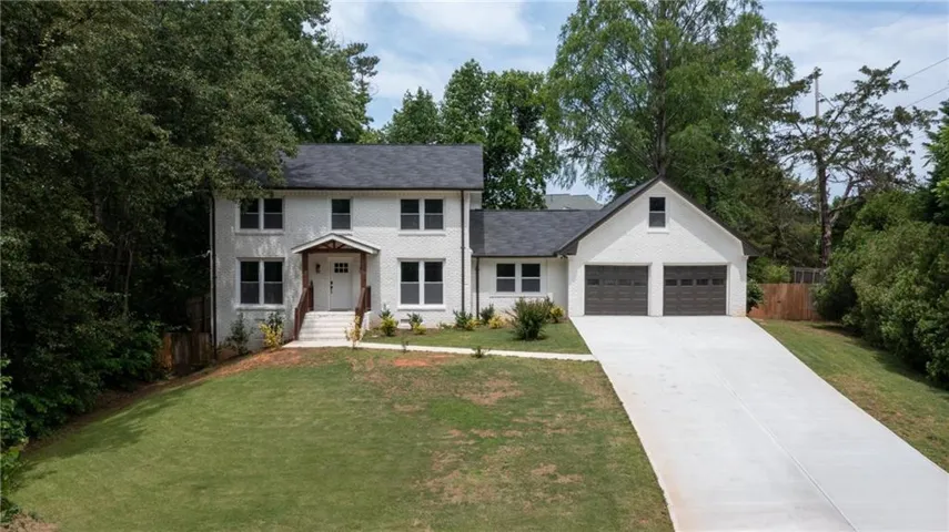 White brick exterior, dark shingle roof, attached two-car garage, wood-tone garage doors, and a concrete driveway