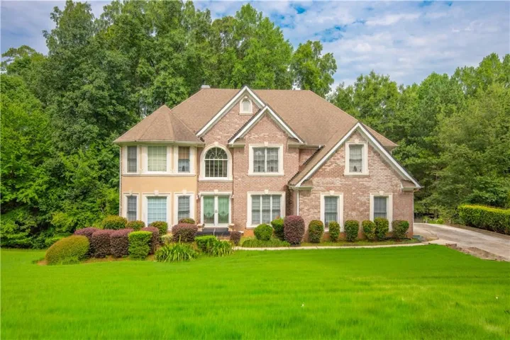 Brick and stucco exterior, gabled roofline, arched window, mature landscaping, and front lawn