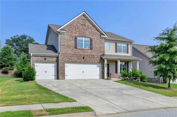 Two-story home featuring a brick and siding exterior, a two-car garage, and a covered front porch