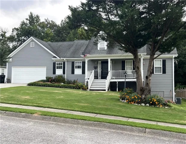 Gray siding exterior with white trim, a covered porch, a two-car garage, and mature landscaping