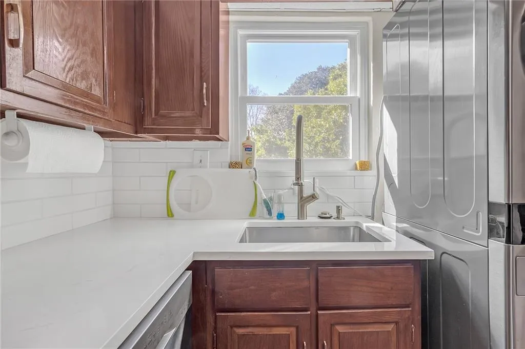Kitchen with tasteful backsplash, stainless steel dishwasher, light stone counters, stacked washing machine and dryer, and wood finish cabinetry