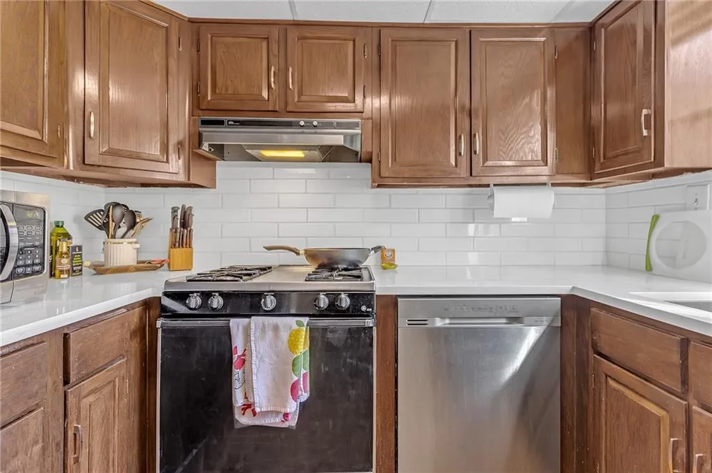 Kitchen featuring stainless steel appliances, tasteful backsplash, wood finish cabinets, and light stone counters