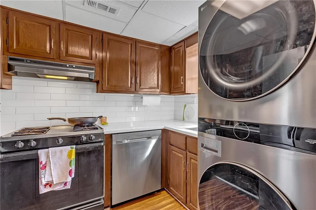Kitchen with wood finish cabinets, range with gas stovetop, tasteful backsplash, dishwasher, and light wood-style floors