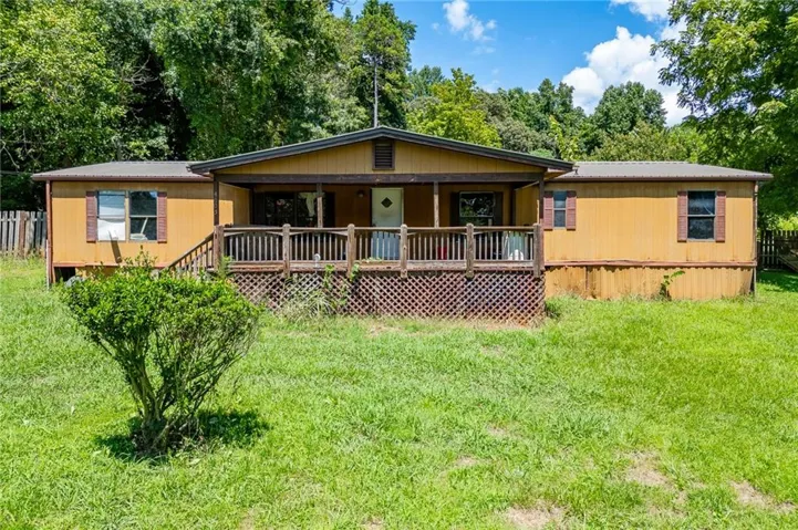 Charming manufactured home featuring a distinctive golden-tan exterior with a spacious covered front porch, lattice skirting, and multi-pane windows