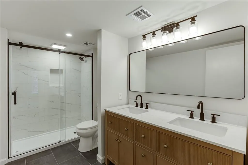 Bathroom with toilet, a sink, a marble finish shower, and visible vents