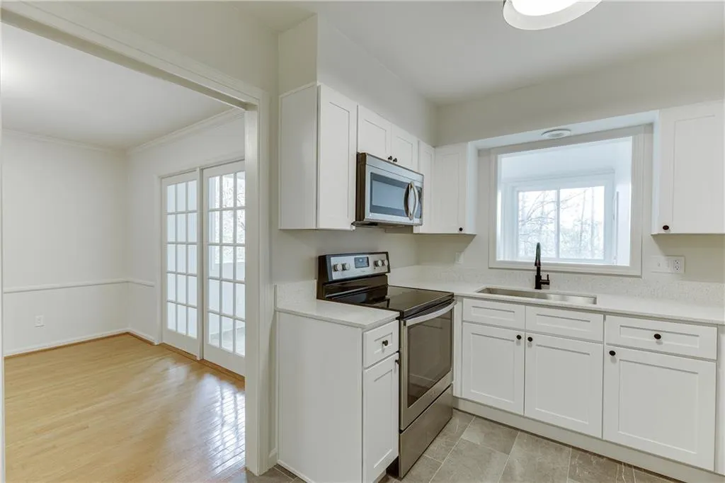 Kitchen featuring light countertops, ornamental molding, appliances with stainless steel finishes, white cabinetry, and a sink