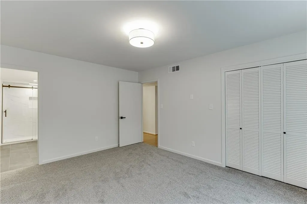 Unfurnished bedroom featuring a closet, ensuite bathroom, visible vents, baseboards, and carpet floors