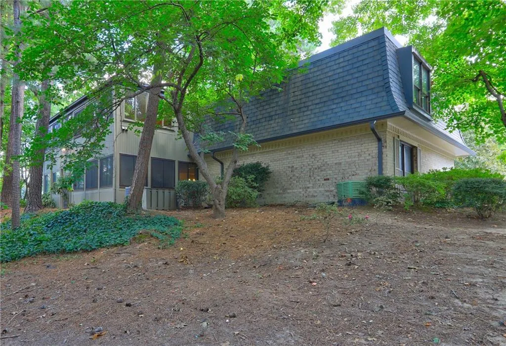 View of home's exterior with mansard roof, brick siding, roof with shingles, and a sunroom