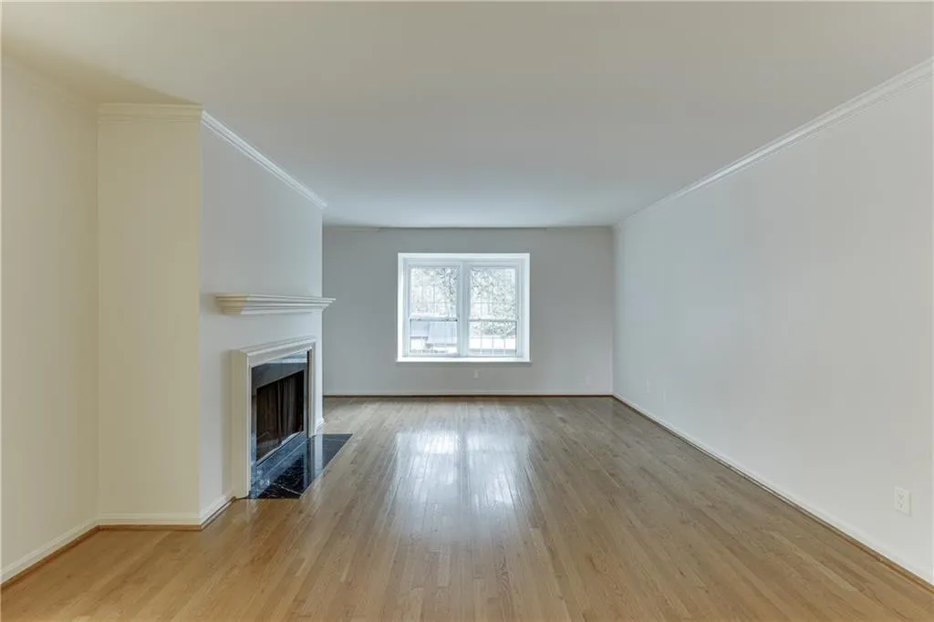 Unfurnished living room with a fireplace with flush hearth, baseboards, crown molding, and light wood-type flooring