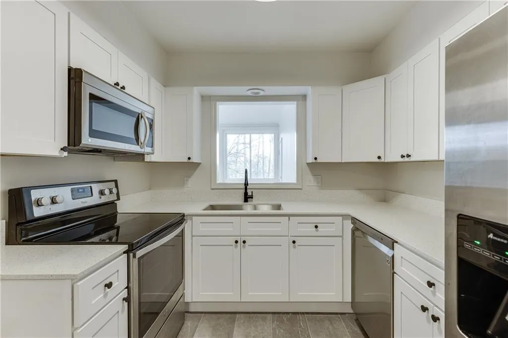 Kitchen with white cabinetry, light countertops, a sink, and stainless steel appliances