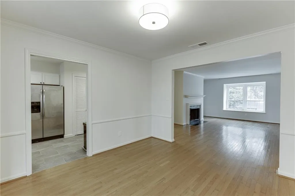 Unfurnished living room with a fireplace with flush hearth, light wood-style flooring, visible vents, and ornamental molding