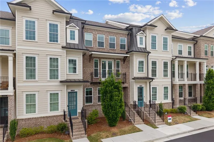 Multi-level townhome featuring a brick and siding exterior, multiple balconies with metal railings, and gabled roof accents