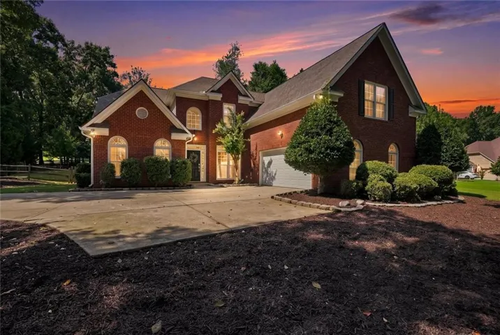 Brick exterior with arched window accents, attached garage, concrete driveway, and mature landscaping