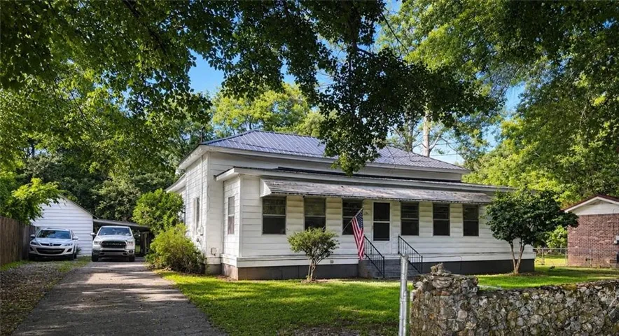 White exterior residence featuring a metal roof, covered front porch, and a stone-faced retaining wall