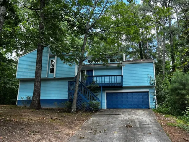 Contemporary exterior featuring light blue siding, a two-car garage, an upper-level balcony, and mature trees