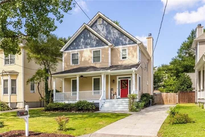 Two-story residence featuring a covered front porch with white railings, a red front door, and a paved driveway