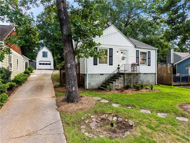 White siding exterior with black shutters, concrete foundation, front porch with black railings, stone steps, and a detached two-car garage